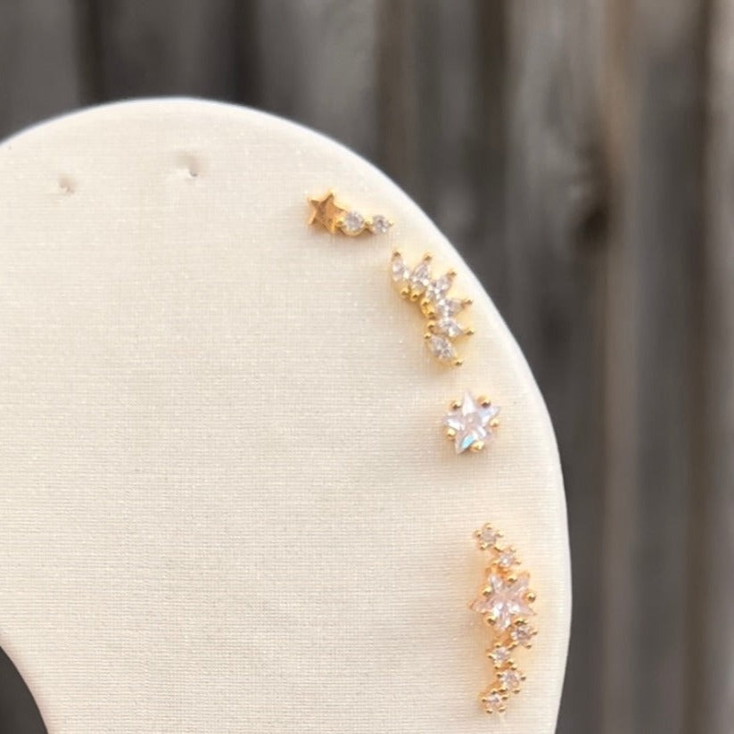 Gold ear studs, listing from top to bottom, shooting star stud, marquise cluster stud, star stud, star constellation stud, star burst stud, teardrop stud, mini hoop and small hoop. 