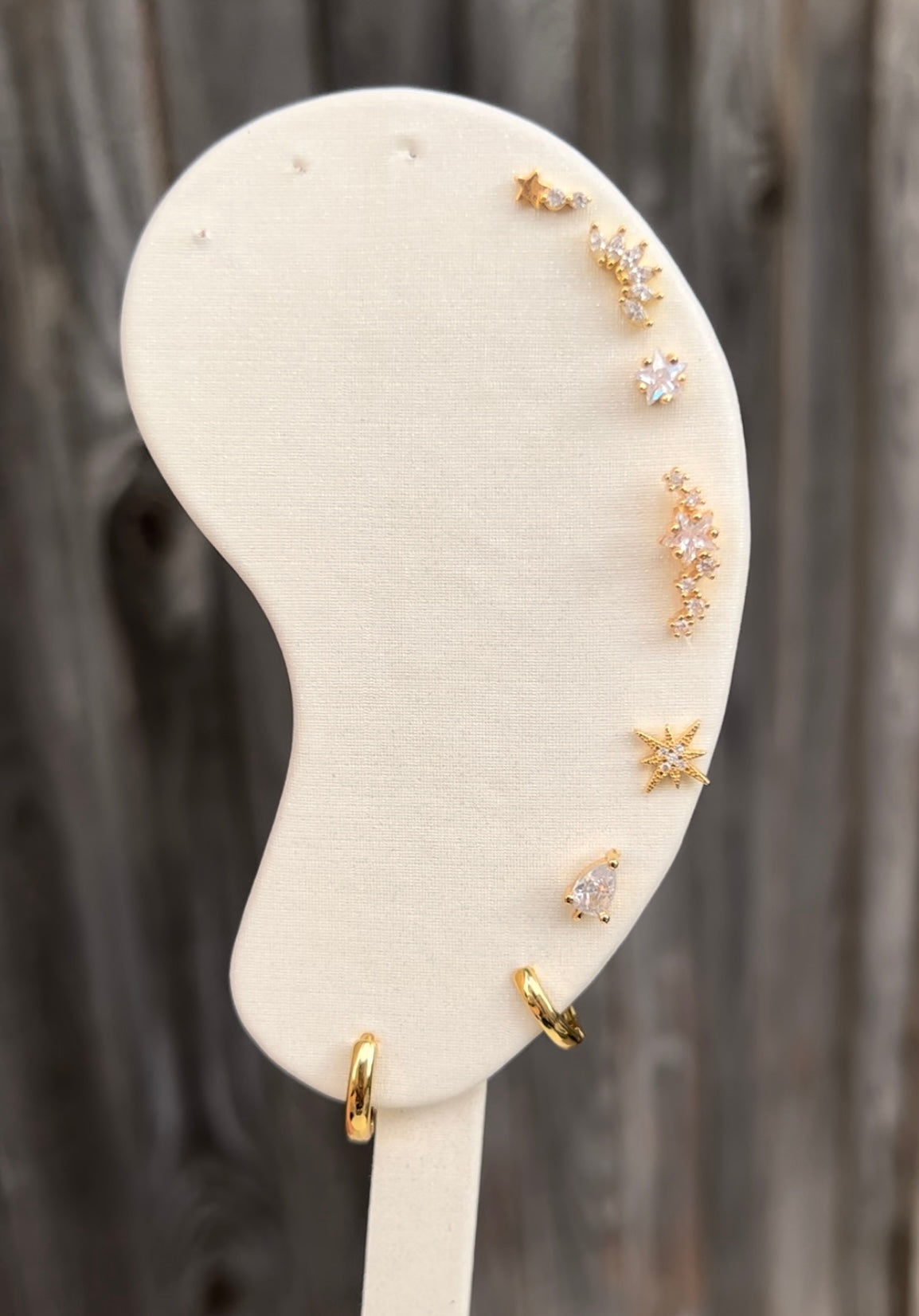 Gold ear studs, listing from top to bottom, shooting star stud, marquise cluster stud, star stud, star constellation stud, star burst stud, teardrop stud, mini hoop and small hoop. 