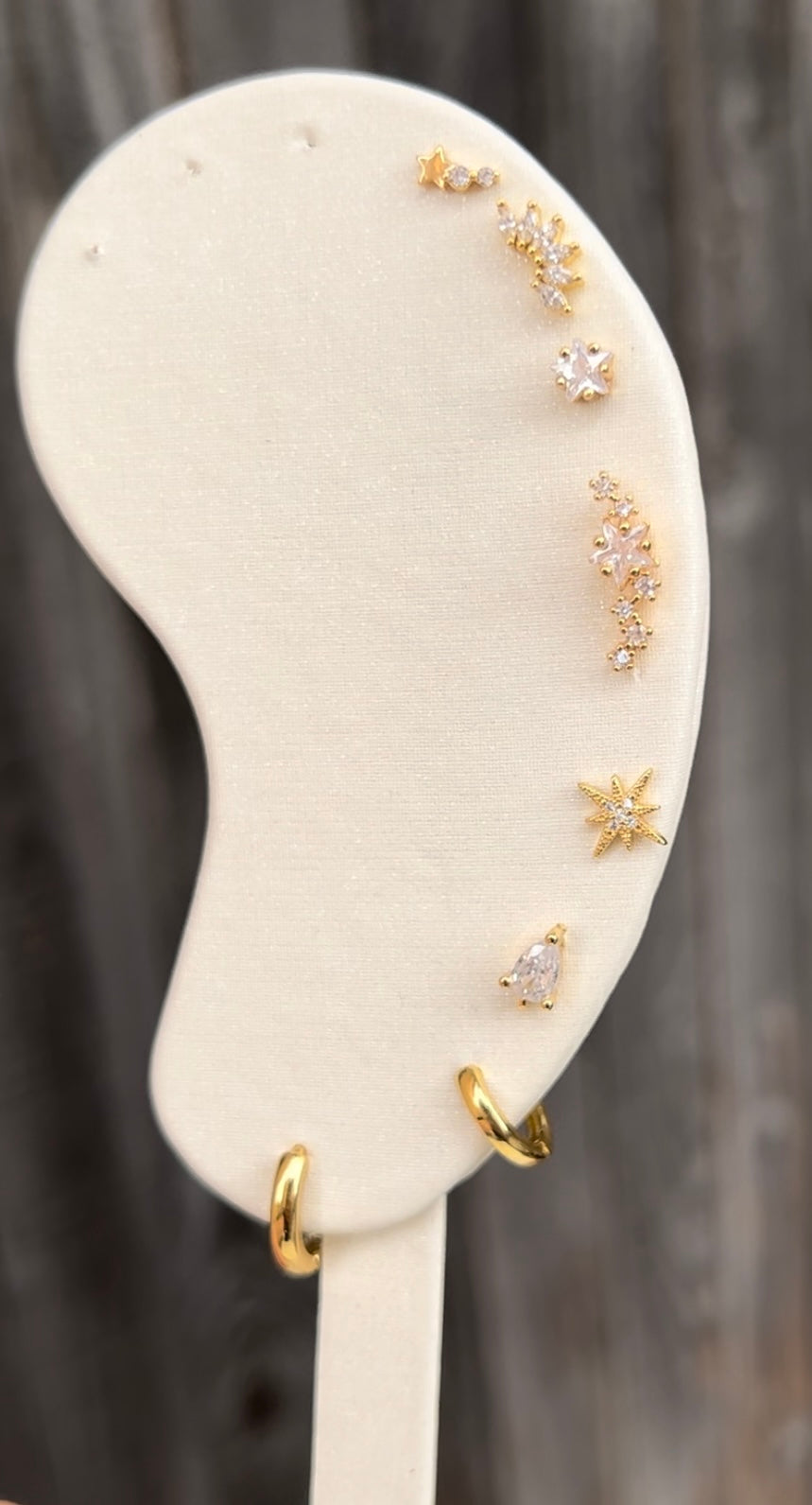 Gold ear studs, listing from top to bottom, shooting star stud, marquise cluster stud, star stud, star constellation stud, star burst stud, teardrop stud, mini hoop and small hoop. 