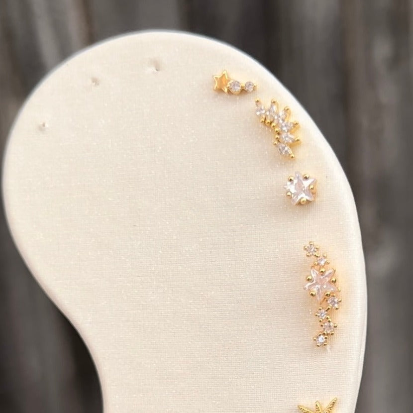 Gold ear studs, listing from top to bottom, shooting star stud, marquise cluster stud, star stud, and star constellation stud.
