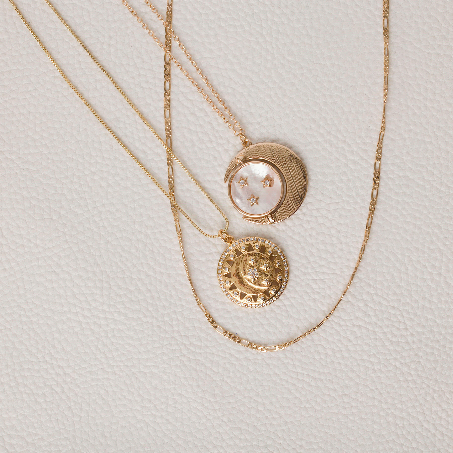 Gold pendant with sun rays, crescent moon and stars. sitting next to a figaro chain and the rotating sun moon and stars necklace